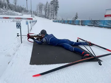 Sportler liegt im Schnee und zielt mit einem Gewehr.