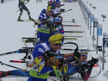 Skifahrer zielen mit Gewehren auf Biathlon-Ski-Strecke im Schnee.