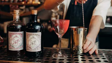 Barkeeper mischt Cocktail, Ginflaschen daneben.