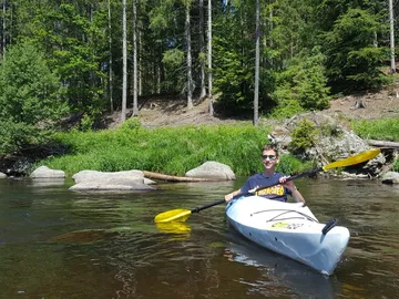 Young man paddles in a kayak on calm water.
