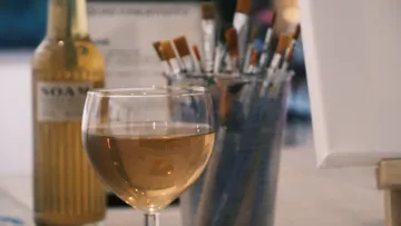 Wine glass, brushes, canvas on table.
