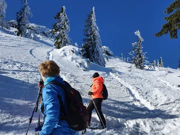 Zwei Menschen wandern im Schnee unter blauem Himmel.