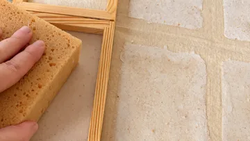 Hand presses sponge on wooden paper mold.