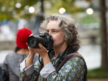 Frau fotografiert mit Kamera in belebtem Außenbereich.