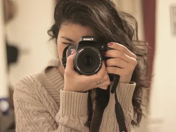 A woman is holding a camera and looking at the viewfinder.
