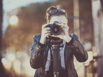 Woman holding camera, taking pictures in an urban environment.