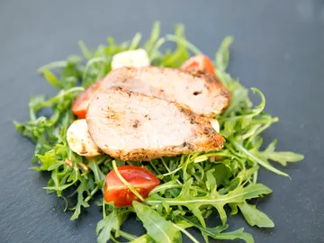 Slice of meat lies on arugula with cherry tomatoes.