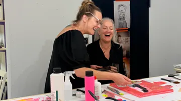 Two women laughing and painting at a table.