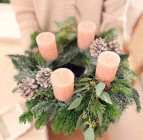Kranz mit rosa Kerzen und Tannenzapfen gezeigt.
