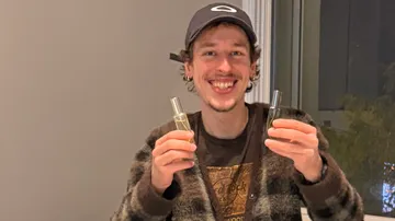 Man holding two perfume bottles indoors.