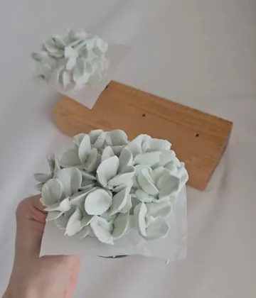 Hand hält weiße Blumenkunst über Tisch.