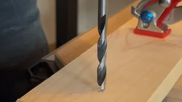Drill bit positioned on wooden plank.