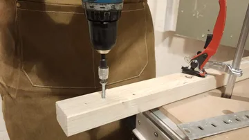 Drill driving screw into wooden plank indoors.
