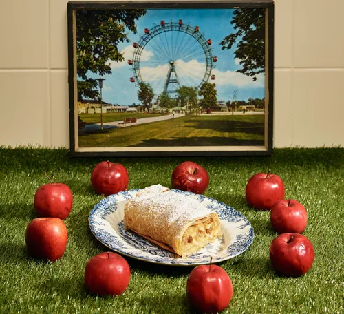 Apfelstrudel liegt auf Teller, umgeben von roten Äpfeln.