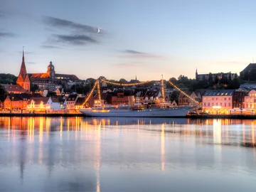 A ship illuminates the water in the harbor at sunset.