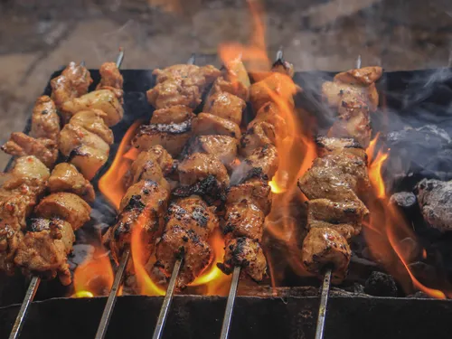 Smoke grilled meat skewers over an open flame.