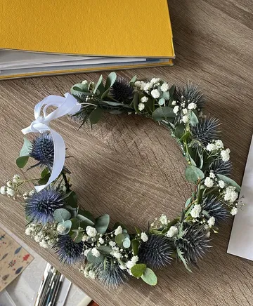 Blumenkranz liegt auf Holztisch neben gelbem Buch.