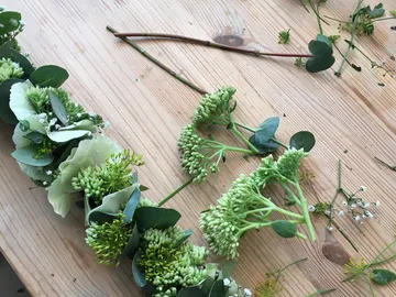 Wreath of flowers on a wooden table surrounded by fresh plants.