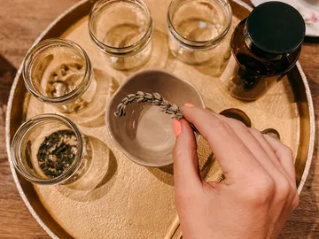 A hand holds lavender over a bowl on a tray.