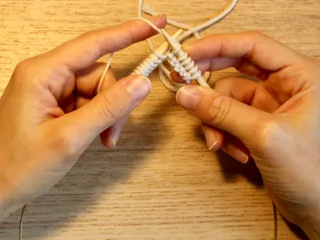 Hände stricken mit Garn auf einem Holzuntergrund.