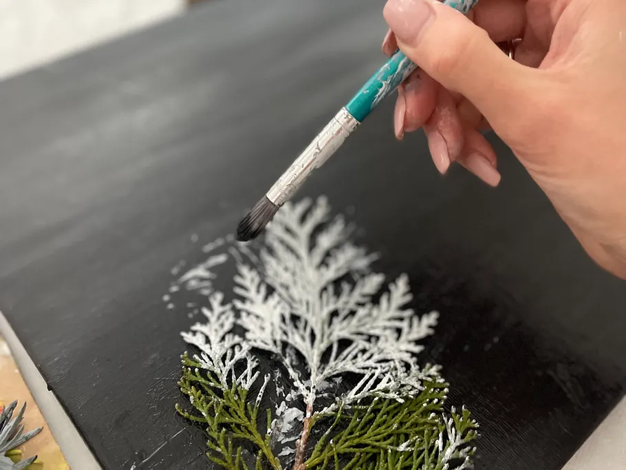 Brush paints white paint on green, plant-like motif.