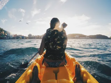 Person paddelt im Kajak auf Wasser bei Sonnenuntergang.
