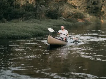 Ein Mann rudert in einem Kanu auf ruhigem Wasser.