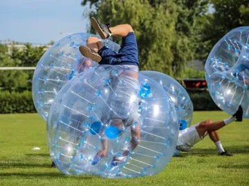 Men roll in large, transparent balls on grass.