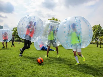 Spieler tragen transparente Bubbles und spielen im Park Fußball.