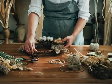 Hands make a wreath of dried flowers on the table.