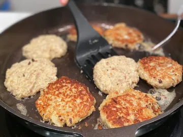 Bratpfanne mit bräunenden Haferflocken-Patties auf dem Herd.