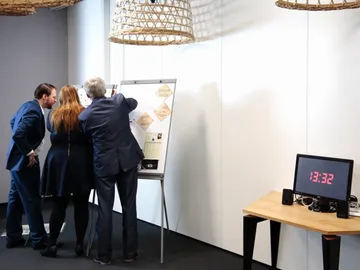 Four people are discussing a flip chart in a modern room.