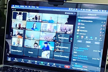 Laptop zeigt Zoom-Meeting mit vielen Teilnehmern auf Bildschirm.