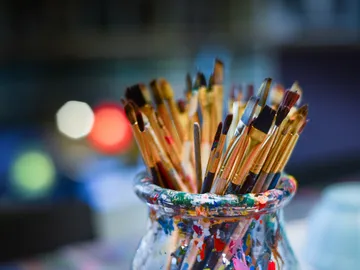 Pinsel stehen in einem bunten Glasbehälter.