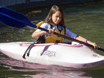 Mädchen paddelt im pinken Kajak auf ruhigem Wasser.