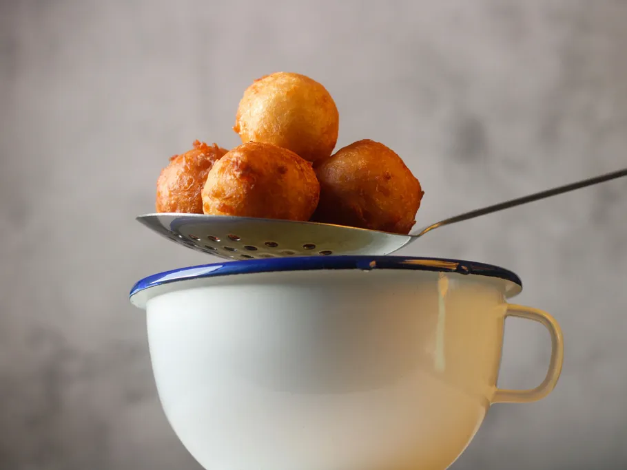 Fried balls are lifted into a bowl with a spoon.