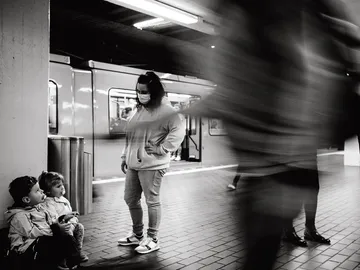 Two children sit on the subway platform; adults are standing.