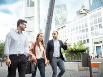 Three people are walking and talking in a city.