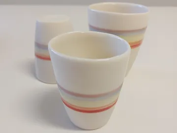 There are three cups on a white table with colorful stripes.