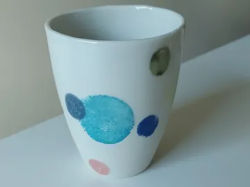 Geometrischer Becher mit bunten Punkten auf weißem Hintergrund.