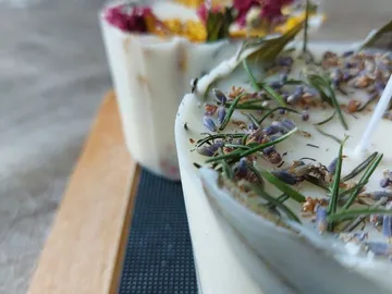 Kerzen mit getrockneten Blumen und Kräutern auf einem Holzbrett.