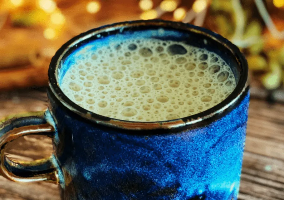 Blauer Becher mit schaumiger Flüssigkeit auf Holzoberfläche.