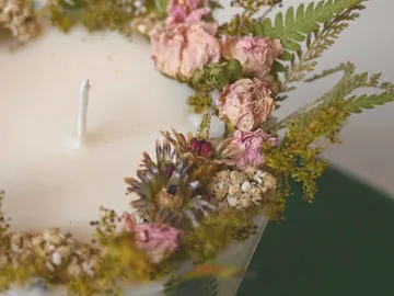 Kerze mit Trockenblumen dekoriert auf hellem Hintergrund.