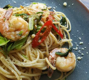 Pasta with shrimp and vegetables on a black plate.