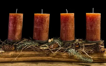 Four candles stand on a piece of wood, surrounded by decoration.