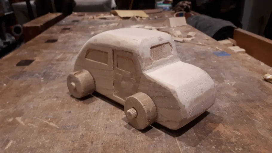 A wooden car is standing on a table in a workshop.