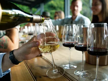 Weinflasche gießt Weißwein in ein Glas, umgeben von Freunden.