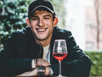 Young man smiles and sits in front of a glass.