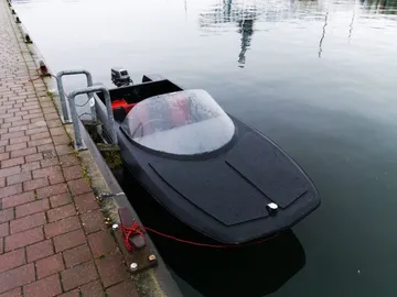 Schwarzes Boot liegt am Steg im ruhigen Wasser.
