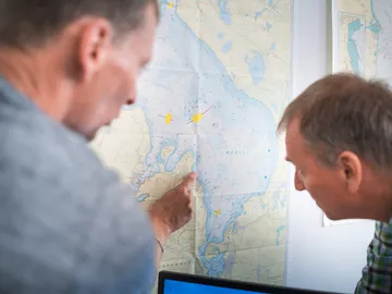 Two men point to a map on the wall.